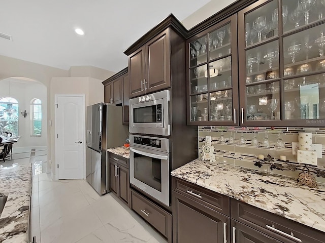 1312 Fishing Lake Dr, Odessa, FL 33556 - kitchen with stainless steel appliances, arched walkways, dark brown cabinets, glass insert cabinets, and light stone counters