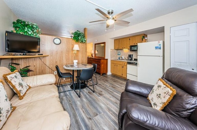 living area featuring light wood-style floors, a textured ceiling, ceiling fan, and wooden walls