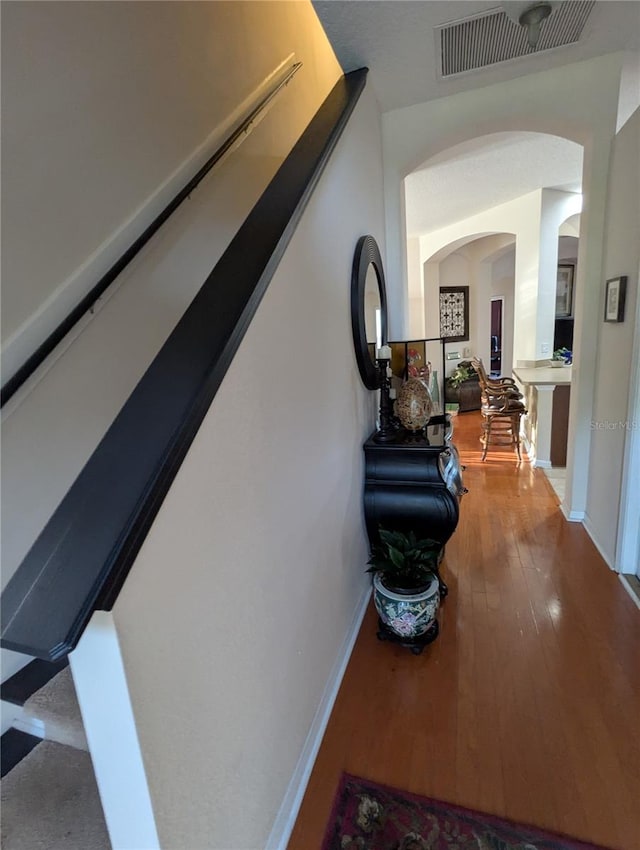 corridor featuring visible vents, hardwood / wood-style floors, baseboards, and arched walkways