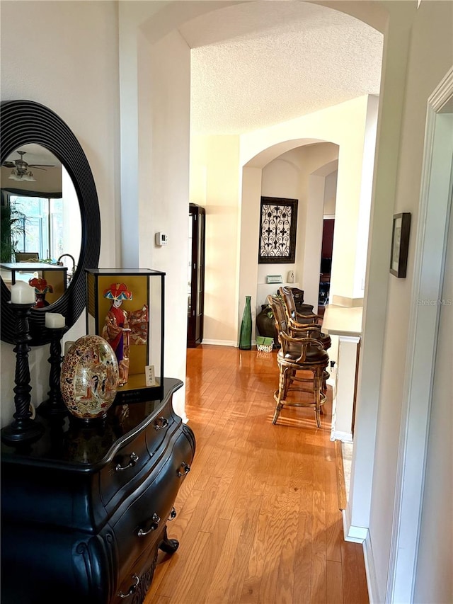 corridor with light wood-type flooring, baseboards, and arched walkways
