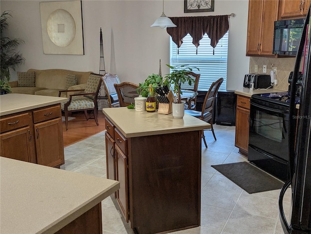 kitchen with brown cabinets, tasteful backsplash, light countertops, a center island, and black appliances