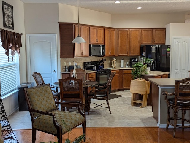 kitchen featuring decorative backsplash, brown cabinetry, black appliances, a center island, and pendant lighting