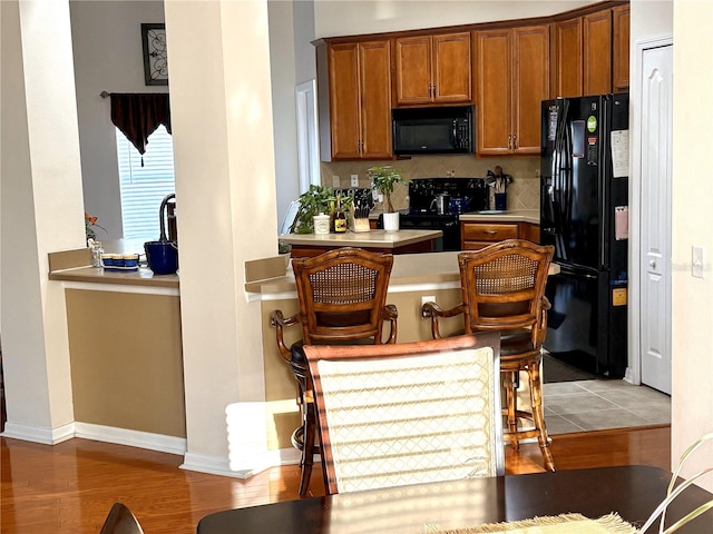 kitchen with light wood-style flooring, light countertops, brown cabinets, black appliances, and backsplash
