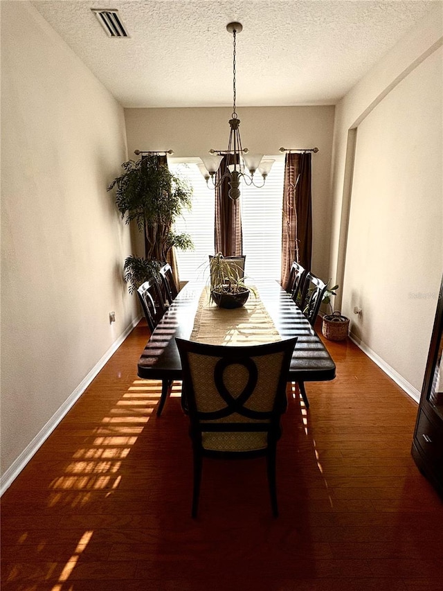 dining area with a chandelier, visible vents, baseboards, a textured ceiling, and wood finished floors