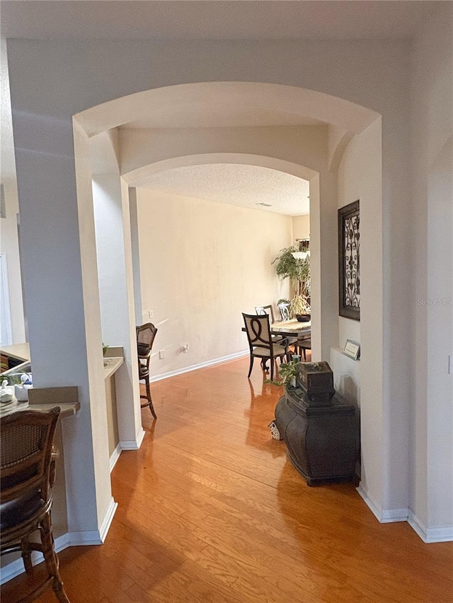 corridor with wood finished floors, baseboards, and arched walkways