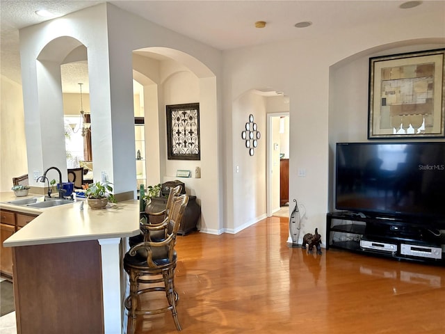 interior space with a sink, light countertops, a breakfast bar, baseboards, and wood finished floors