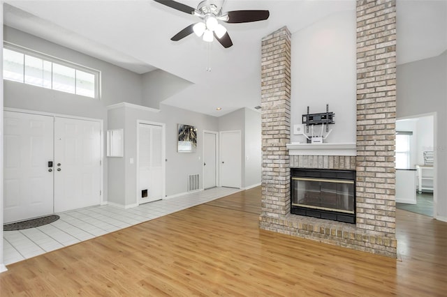 unfurnished living room with visible vents, wood finished floors, a brick fireplace, ceiling fan, and high vaulted ceiling