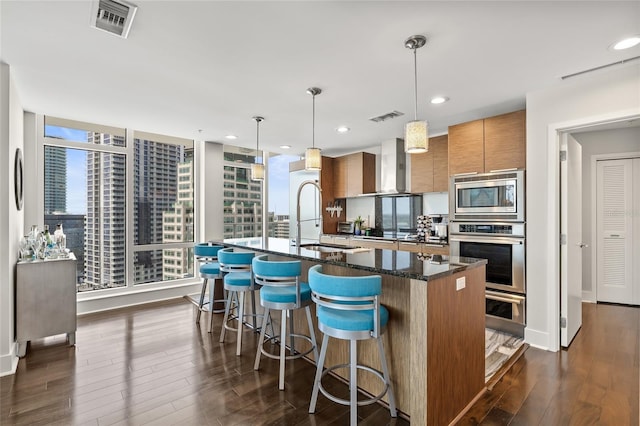 175 1st St S Unit 2603, Saint Petersburg, FL 33701 - kitchen featuring brown cabinetry, appliances with stainless steel finishes, dark wood-style flooring, a sink, and wall chimney exhaust hood