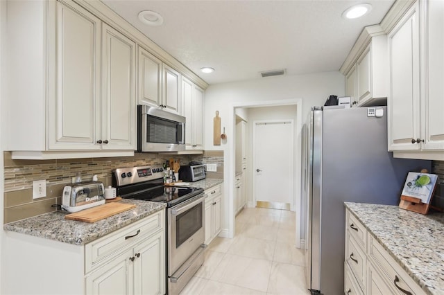 kitchen with stainless steel appliances, visible vents, backsplash, light stone countertops, and baseboards