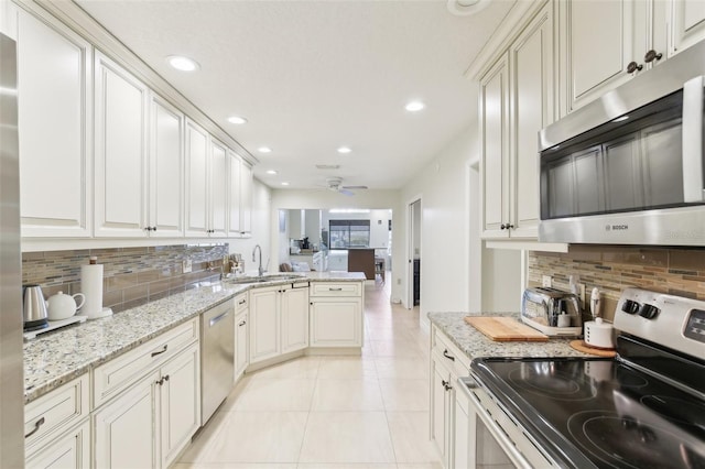 kitchen featuring stainless steel appliances, a peninsula, decorative backsplash, and a sink