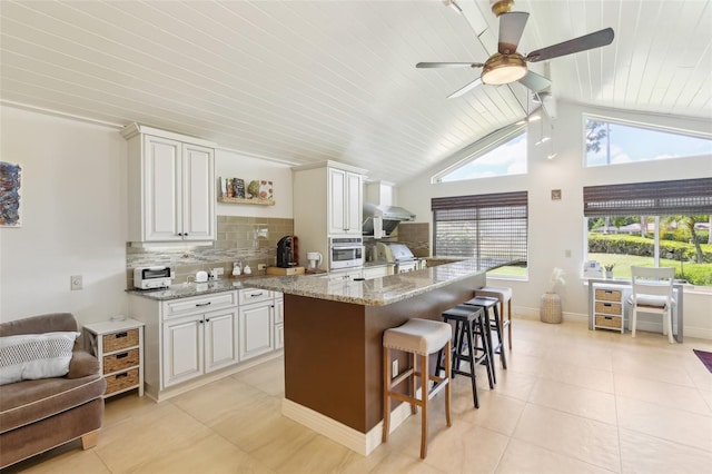 kitchen with light tile patterned floors, a ceiling fan, a kitchen breakfast bar, backsplash, and stainless steel oven