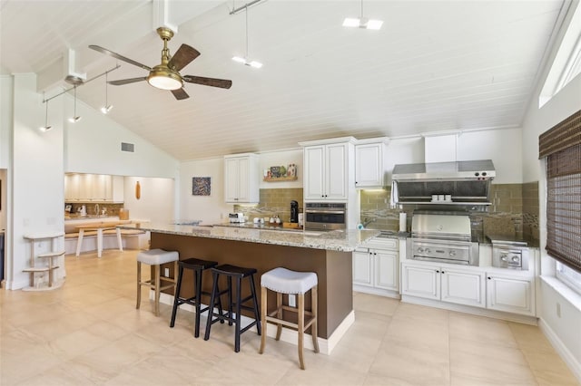 kitchen featuring a ceiling fan, stainless steel oven, visible vents, a kitchen bar, and decorative backsplash