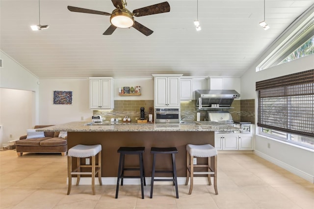 kitchen featuring stainless steel oven, tasteful backsplash, a kitchen bar, and vaulted ceiling