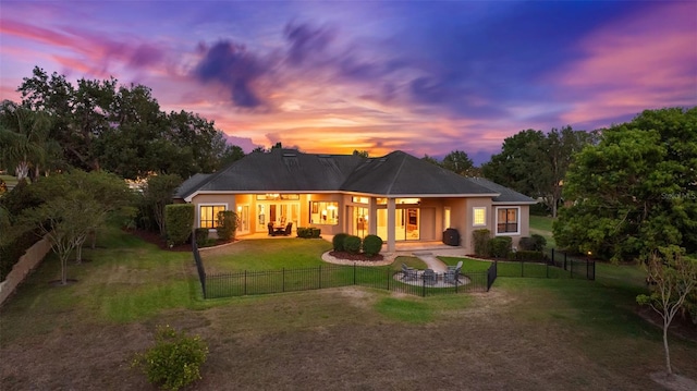 back of house at dusk featuring a lawn, a patio, stucco siding, and a fenced backyard