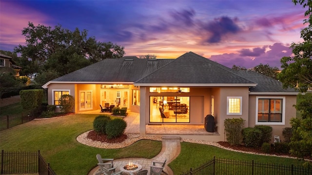 back of house at dusk featuring a patio, fence private yard, stucco siding, a lawn, and a fire pit