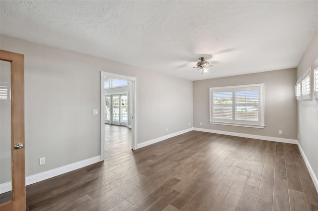 17 Bellevue Dr, Treasure Island, FL 33706 - empty room with dark wood finished floors, ceiling fan, plenty of natural light, baseboards, and a textured ceiling