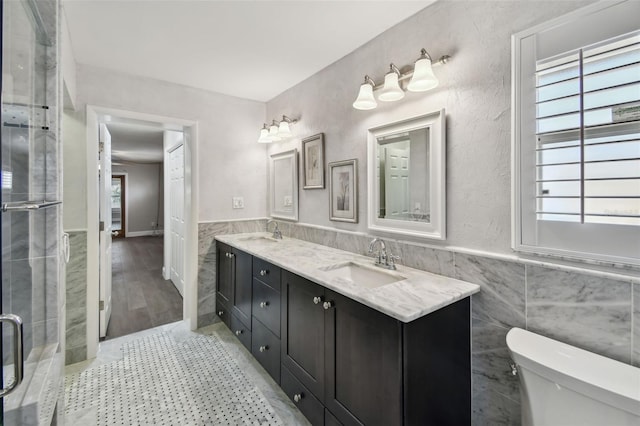 17 Bellevue Dr, Treasure Island, FL 33706 - full bath featuring tile walls, double vanity, toilet, a wainscoted wall, and tiled shower