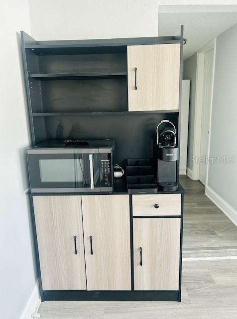 6401 30th Way N, Saint Petersburg, FL 33702 - kitchen featuring light brown cabinetry, open shelves, wood finished floors, stainless steel microwave, and baseboards