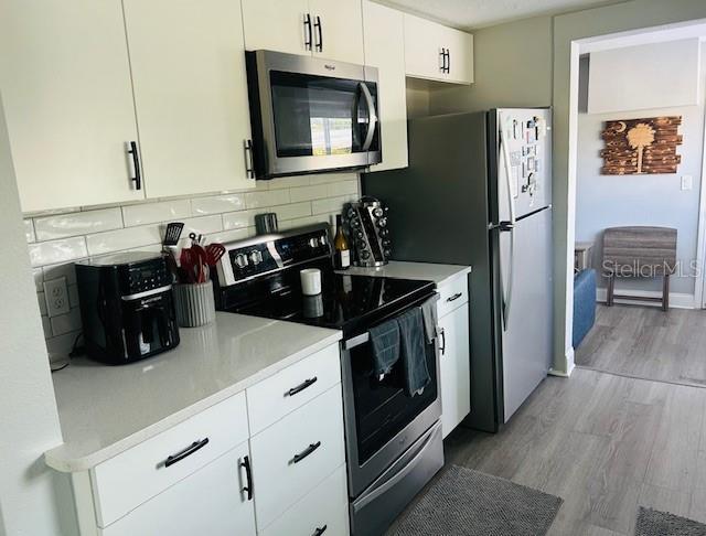 6401 30th Way N, Saint Petersburg, FL 33702 - kitchen featuring light countertops, light wood-style flooring, tasteful backsplash, appliances with stainless steel finishes, and white cabinetry