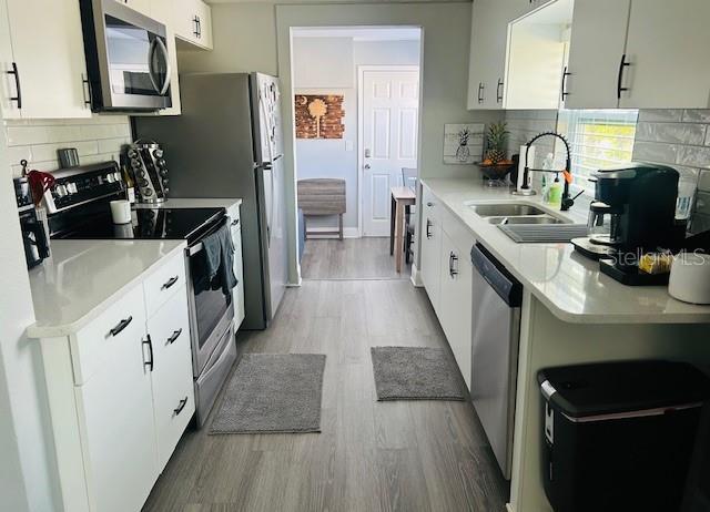 6401 30th Way N, Saint Petersburg, FL 33702 - kitchen featuring stainless steel appliances, light wood-style flooring, a sink, decorative backsplash, and light countertops