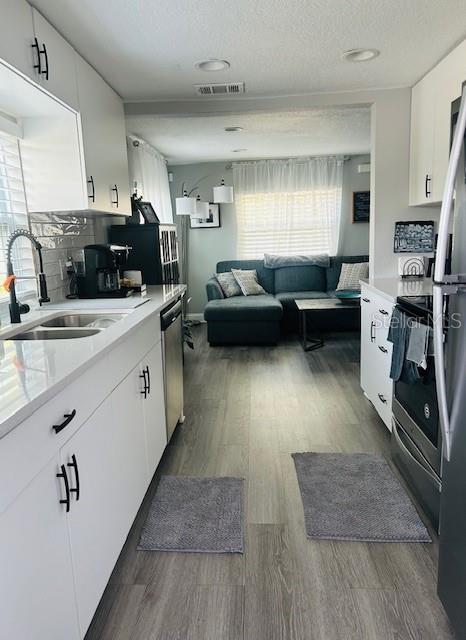 6401 30th Way N, Saint Petersburg, FL 33702 - kitchen featuring dark wood-style floors, stainless steel appliances, light countertops, a sink, and white cabinetry