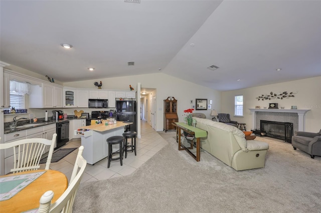 living area featuring light tile patterned floors, light colored carpet, visible vents, vaulted ceiling, and a fireplace