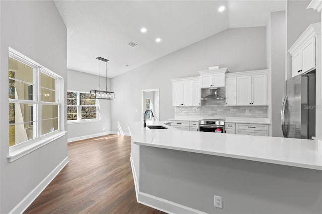 kitchen with wall chimney exhaust hood, white cabinetry, a sink, appliances with stainless steel finishes, and backsplash
