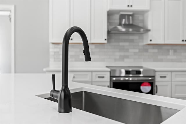 kitchen featuring decorative backsplash, wall chimney range hood, light countertops, white cabinetry, and range