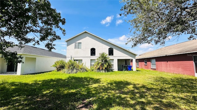 rear view of house featuring a lawn and stucco siding