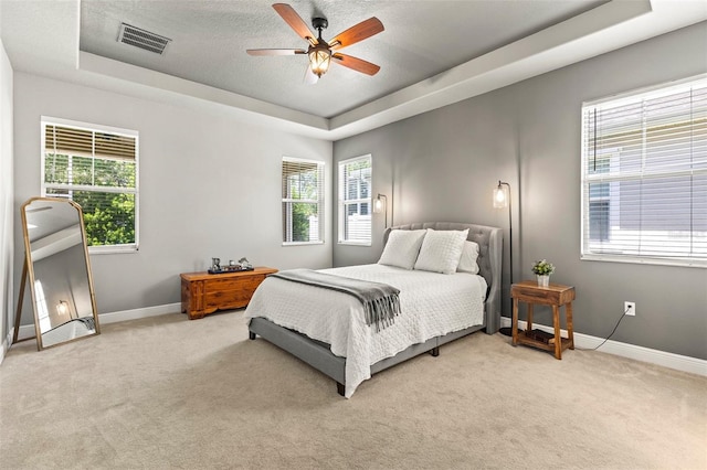 bedroom with visible vents, baseboards, a tray ceiling, and light carpet