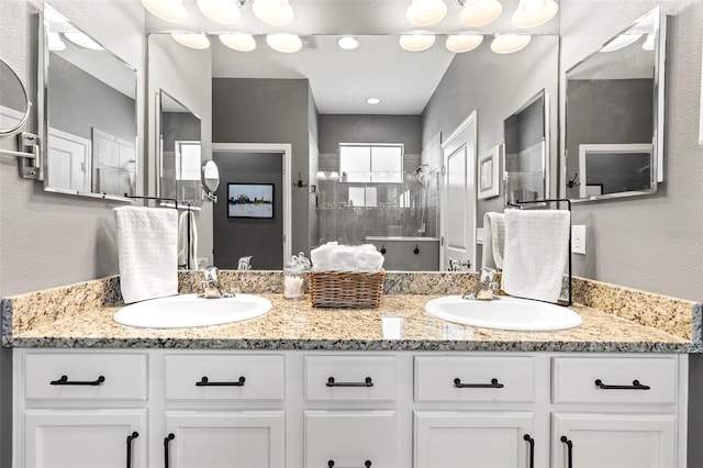 full bathroom with double vanity, walk in shower, and a sink