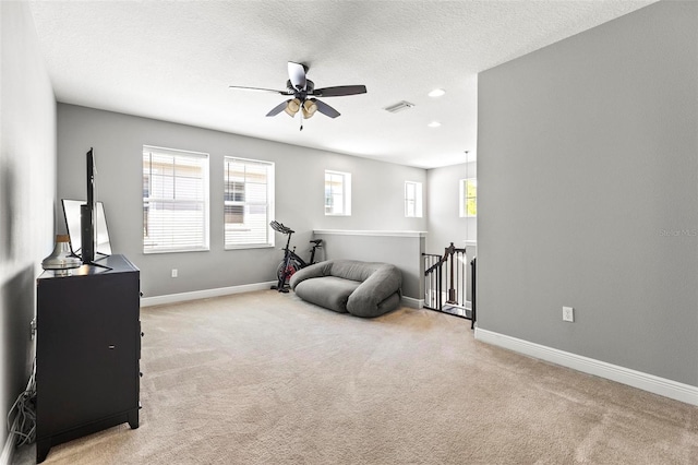 living area with visible vents, a ceiling fan, light carpet, and an upstairs landing