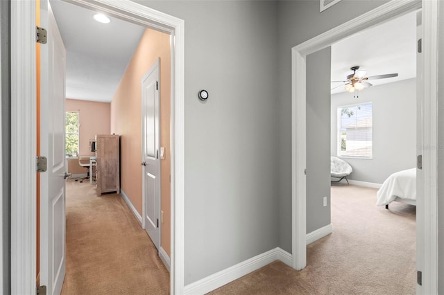 corridor with baseboards, light colored carpet, and a healthy amount of sunlight