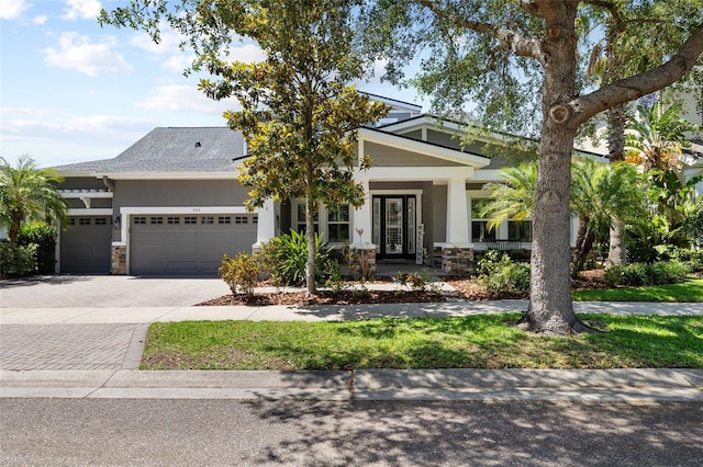 craftsman house with a garage, decorative driveway, stone siding, and a porch