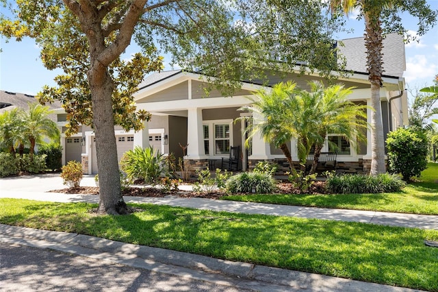 view of front of home featuring covered porch, driveway, a front yard, a garage, and stone siding
