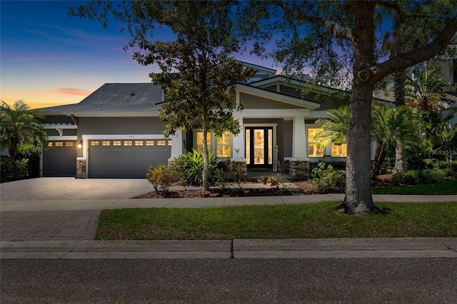 craftsman house with a garage, decorative driveway, stucco siding, and stone siding
