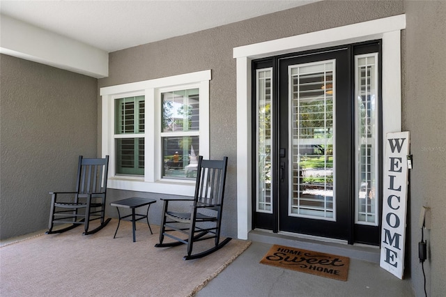 entrance to property with a porch and stucco siding