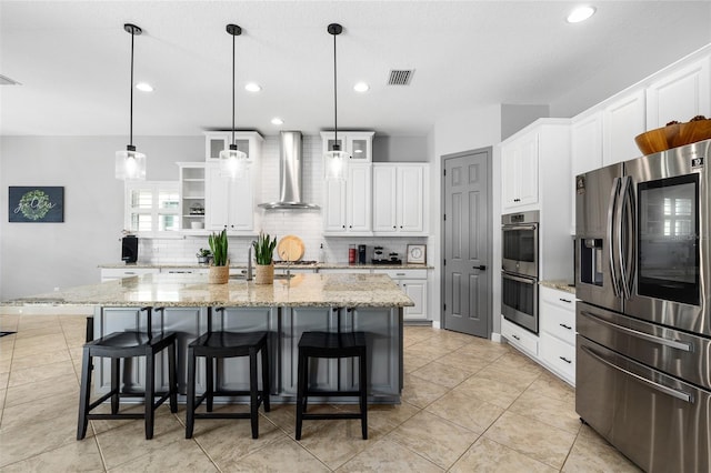 kitchen with white cabinets, appliances with stainless steel finishes, wall chimney exhaust hood, decorative backsplash, and visible vents