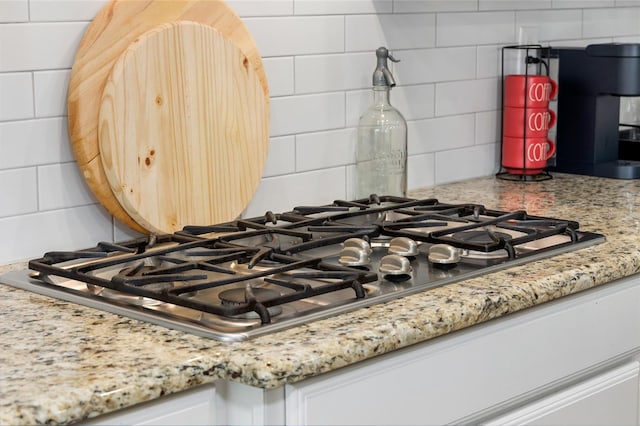 details featuring white cabinetry, backsplash, light stone countertops, and stainless steel gas stovetop