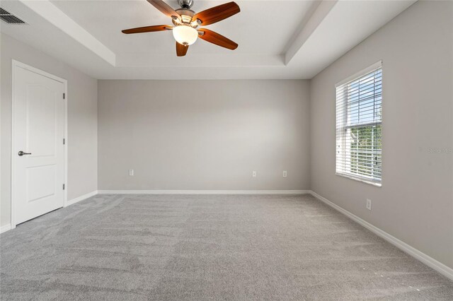 empty room featuring a tray ceiling, carpet floors, visible vents, and ceiling fan