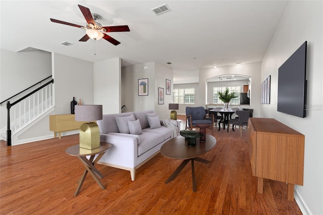 living area featuring visible vents, a ceiling fan, wood finished floors, and stairs