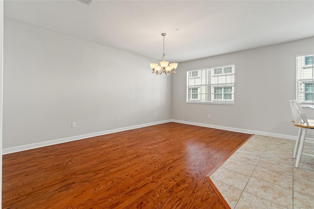 empty room with baseboards, an inviting chandelier, and light wood-style floors