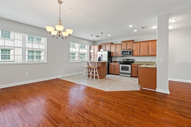 kitchen featuring a sink, stainless steel appliances, an inviting chandelier, a kitchen bar, and light wood-type flooring