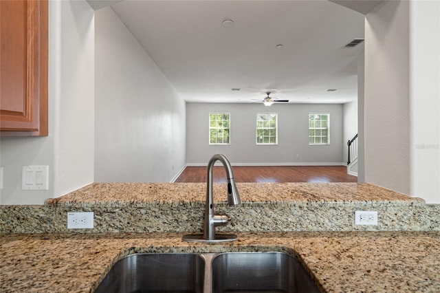 kitchen featuring light stone counters, wood finished floors, visible vents, a ceiling fan, and a sink