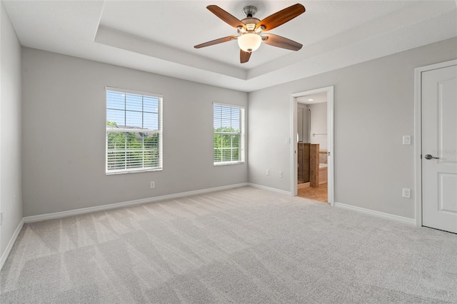 unfurnished bedroom with connected bathroom, carpet flooring, a raised ceiling, baseboards, and a ceiling fan