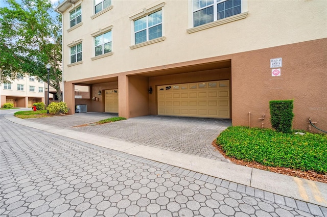exterior space with an attached garage, central AC unit, decorative driveway, and stucco siding