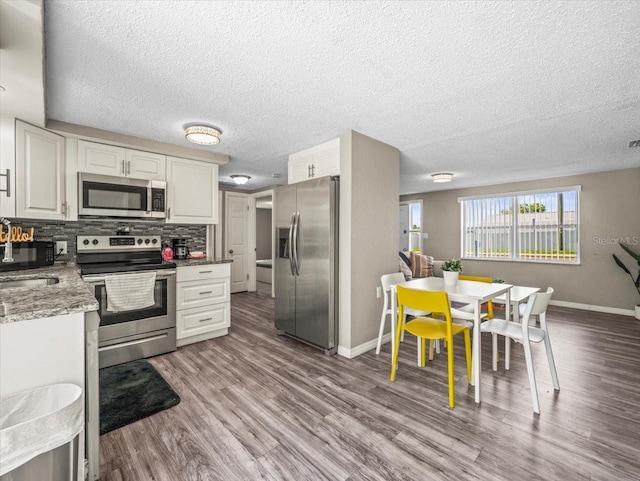 kitchen with appliances with stainless steel finishes, baseboards, white cabinets, wood finished floors, and a textured ceiling