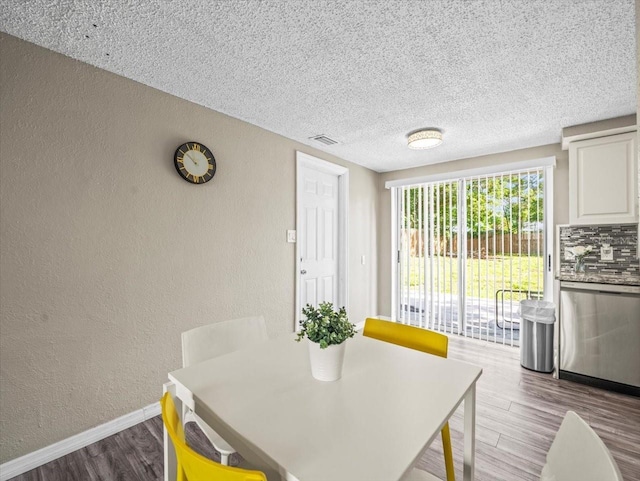 dining area with a textured wall, wood finished floors, baseboards, and a textured ceiling