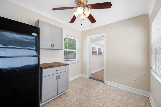 kitchen featuring light speckled floor, baseboards, freestanding refrigerator, butcher block countertops, and gray cabinets