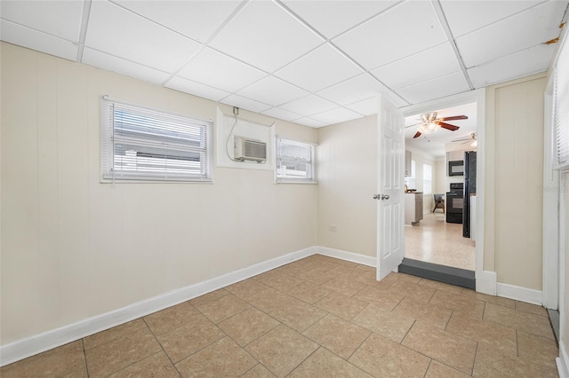 unfurnished room with a wall mounted air conditioner, a ceiling fan, baseboards, and a paneled ceiling